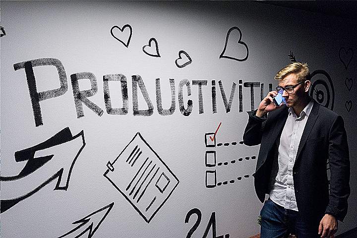 man holding smartphone looking at productivity wall decor