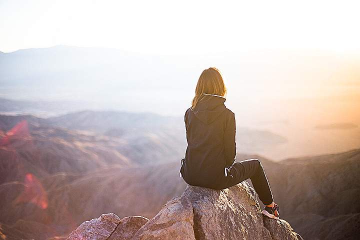 person sitting on top of gray rock overlooking mountain during daytime