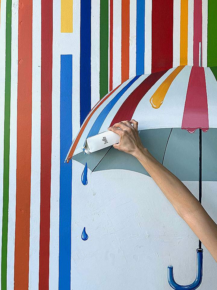 a person holding an umbrella in front of a colorful wall
